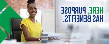 A picture of an employee working at a desk and smiling in a yellow shirt and a brick wall in the background, with text overlaid that says 